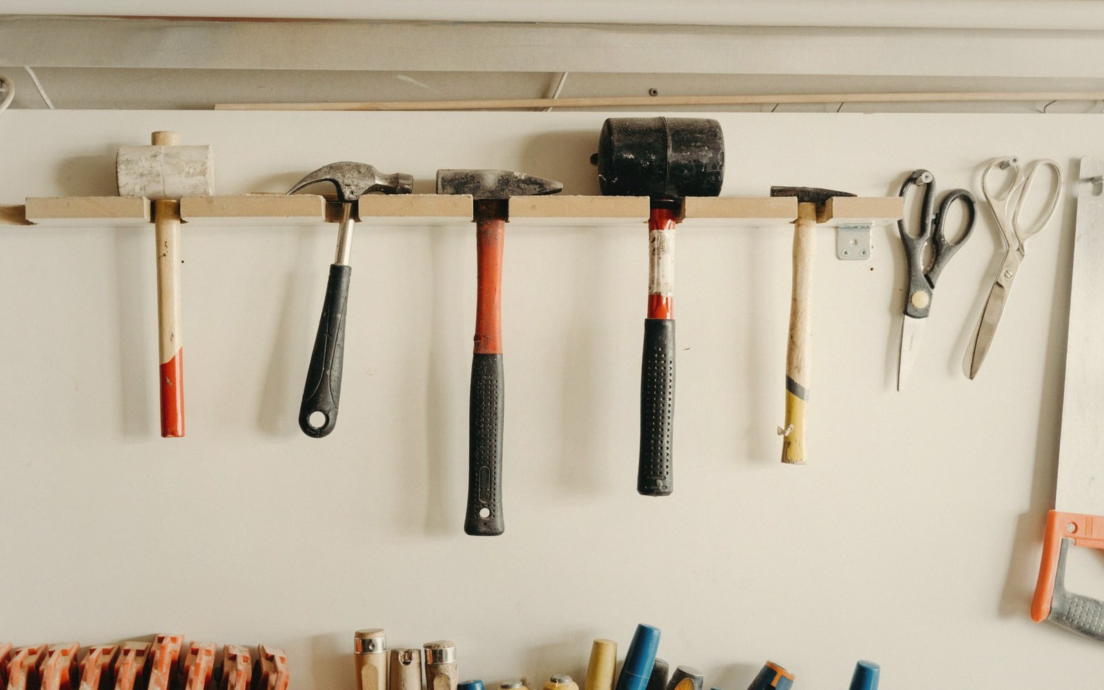 Various hammers, scissors and a hacksaw hang from a wooden rack on a wall